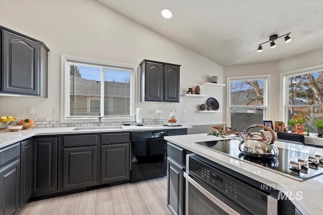 kitchen with light countertops, lofted ceiling, light wood-style floors, black appliances, and a sink