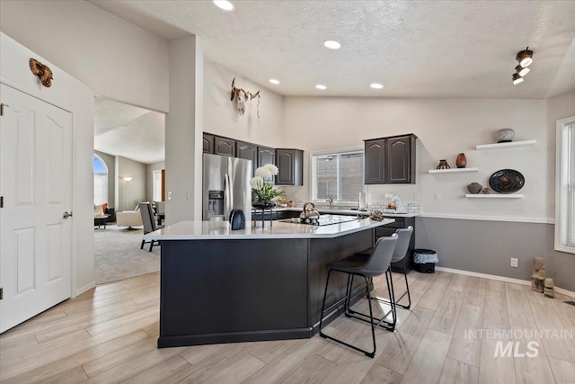 kitchen featuring a center island with sink, light countertops, vaulted ceiling, light wood-style floors, and stainless steel refrigerator with ice dispenser