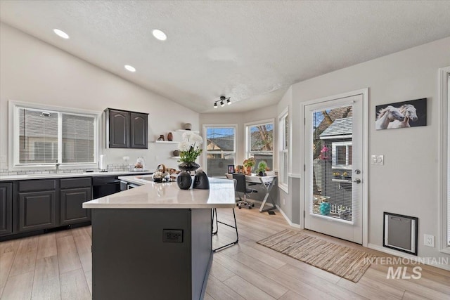 kitchen featuring a center island, light countertops, light wood-type flooring, vaulted ceiling, and a sink