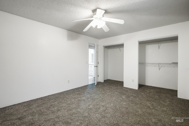 unfurnished bedroom featuring multiple closets, ceiling fan, a textured ceiling, and dark colored carpet