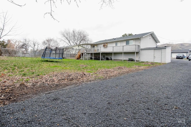 view of home's exterior featuring a trampoline, a deck, a storage shed, and a lawn