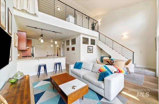living room with a towering ceiling, light wood-style floors, baseboards, stairway, and rail lighting