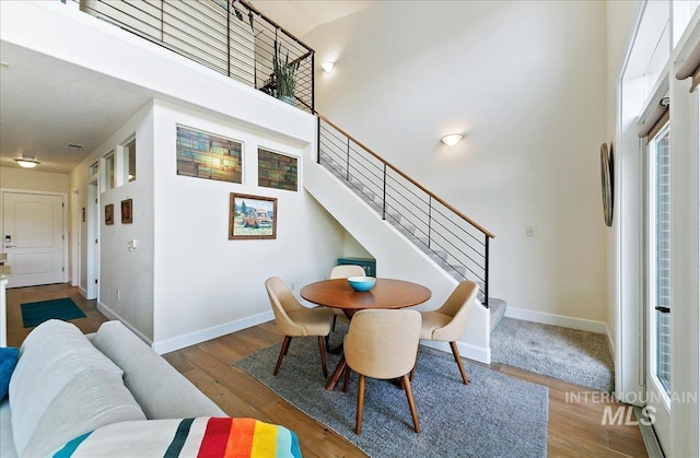 dining space with baseboards, a towering ceiling, wood finished floors, and stairway
