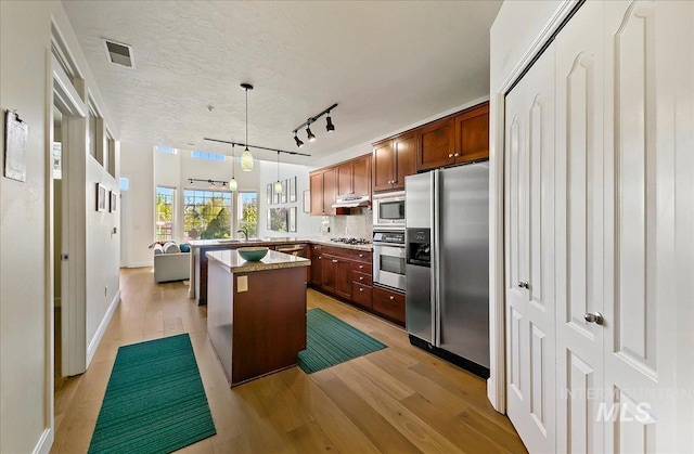 kitchen with appliances with stainless steel finishes, a sink, light wood finished floors, a kitchen island, and visible vents