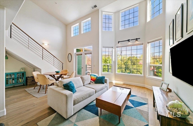 living area featuring baseboards, visible vents, wood finished floors, and a towering ceiling