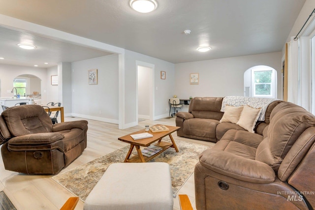 living room with arched walkways, a healthy amount of sunlight, light wood finished floors, and baseboards