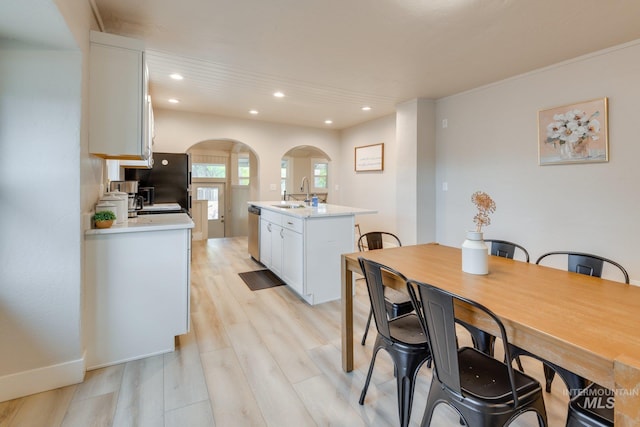 dining area featuring arched walkways, light wood finished floors, and recessed lighting