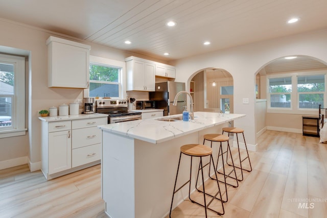 kitchen featuring a sink, a kitchen island with sink, a breakfast bar, light wood-style flooring, and appliances with stainless steel finishes