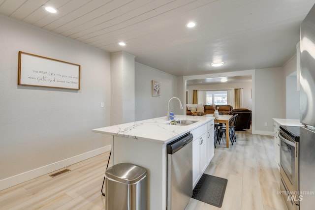 kitchen featuring stainless steel appliances, a kitchen island with sink, a sink, light wood-type flooring, and visible vents
