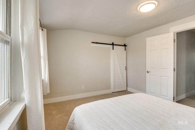 bedroom featuring lofted ceiling, baseboards, light colored carpet, and a barn door