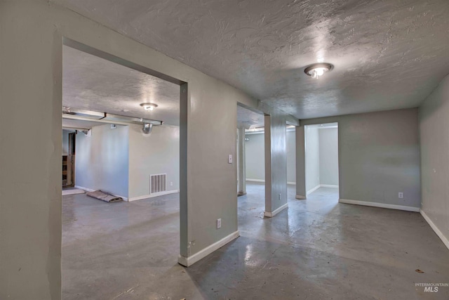 empty room with concrete floors, a textured ceiling, visible vents, and baseboards