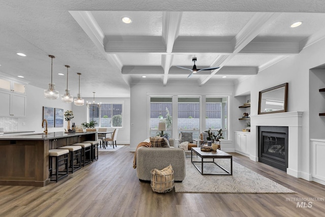 living room with coffered ceiling, light hardwood / wood-style flooring, beamed ceiling, a textured ceiling, and ceiling fan with notable chandelier