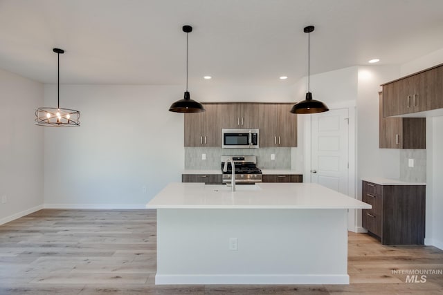 kitchen with light hardwood / wood-style floors, stainless steel appliances, pendant lighting, and backsplash