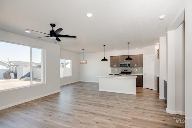 kitchen with light hardwood / wood-style floors, hanging light fixtures, a kitchen island with sink, backsplash, and stainless steel appliances