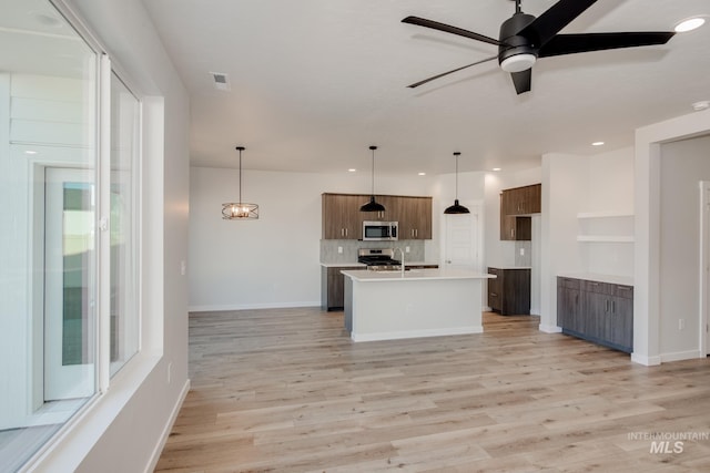 kitchen featuring light hardwood / wood-style floors, a kitchen island with sink, hanging light fixtures, and appliances with stainless steel finishes