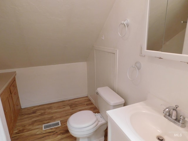 bathroom with visible vents, toilet, vanity, wood finished floors, and lofted ceiling