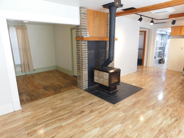 unfurnished living room featuring wood finished floors, a wood stove, and rail lighting