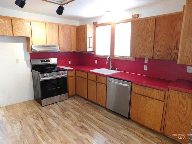 kitchen with a sink, light wood-style floors, under cabinet range hood, brown cabinets, and stainless steel appliances