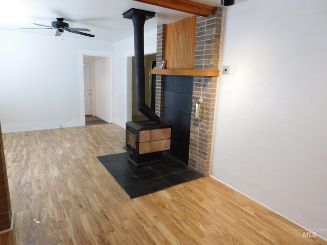 unfurnished living room featuring wood finished floors, a wood stove, baseboards, and a ceiling fan