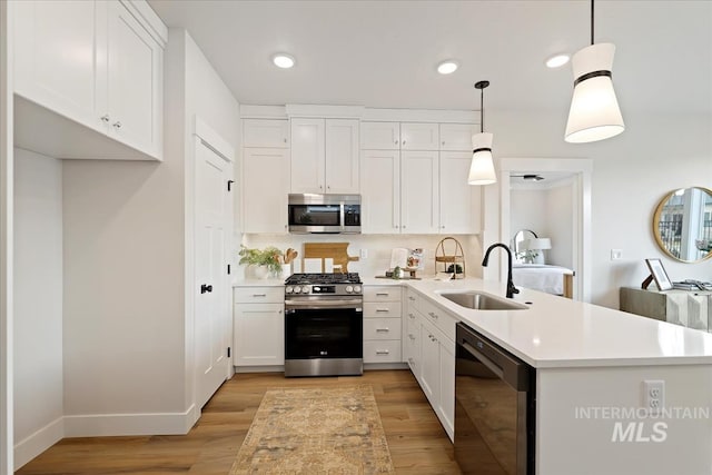 kitchen with light countertops, appliances with stainless steel finishes, a peninsula, white cabinets, and a sink