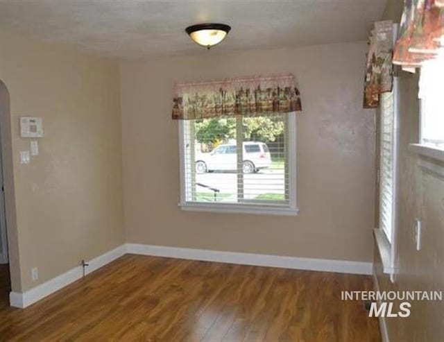 unfurnished dining area featuring arched walkways, a healthy amount of sunlight, baseboards, and wood finished floors