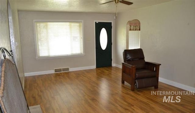 living area featuring ceiling fan, visible vents, baseboards, and wood finished floors