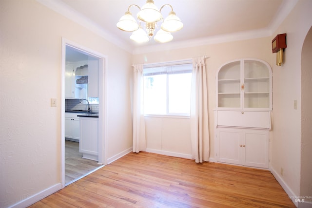 unfurnished dining area with built in features, light hardwood / wood-style flooring, a chandelier, and ornamental molding