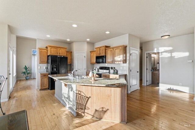 kitchen with black appliances, an island with sink, light stone countertops, light wood finished floors, and recessed lighting