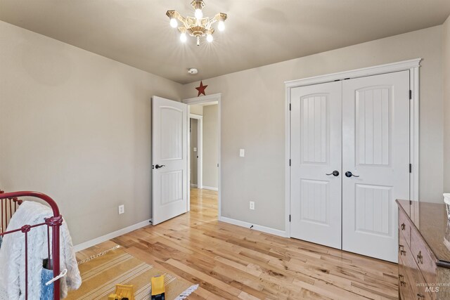 unfurnished bedroom featuring light wood-style floors, baseboards, a closet, and a chandelier