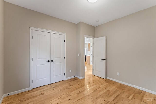unfurnished bedroom with light wood-style flooring, baseboards, and a closet