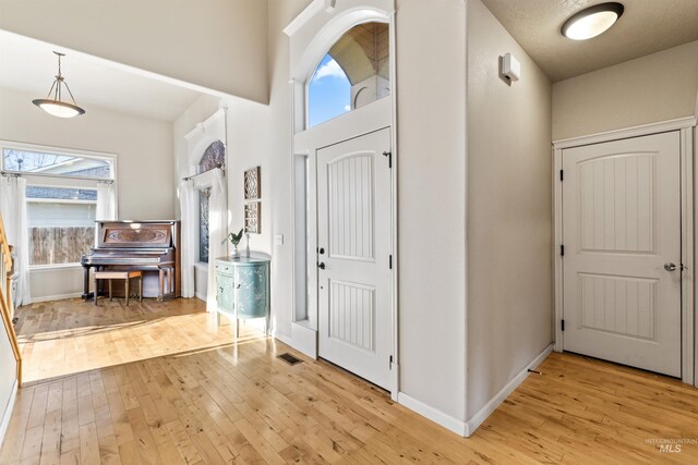 foyer with light wood finished floors, baseboards, and a high ceiling