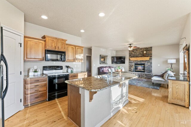 kitchen featuring black microwave, electric range, a stone fireplace, open floor plan, and ceiling fan