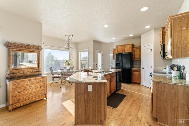 kitchen featuring a sink, black appliances, a textured ceiling, a kitchen island with sink, and a chandelier