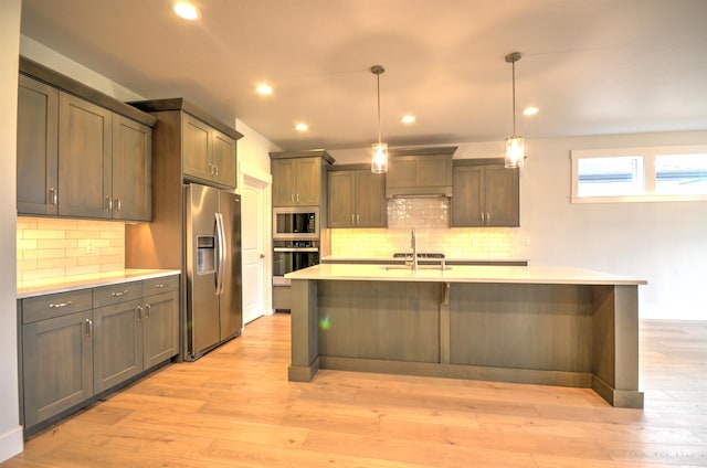 kitchen with pendant lighting, a kitchen island with sink, light wood-type flooring, tasteful backsplash, and stainless steel appliances