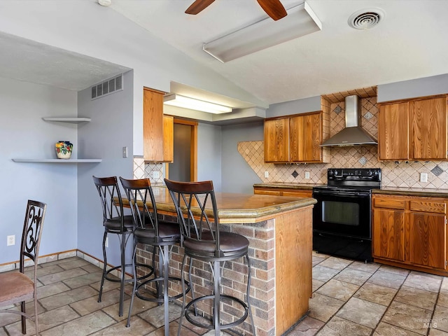 1872 E 1750 S, Gooding, ID 83330 - kitchen featuring wall chimney exhaust hood, black range with electric stovetop, brown cabinets, stone tile flooring, and decorative backsplash