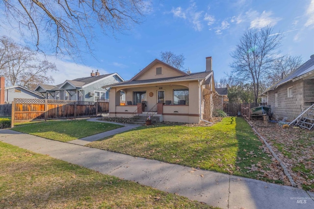 bungalow-style home with covered porch, fence, stucco siding, a chimney, and a front yard