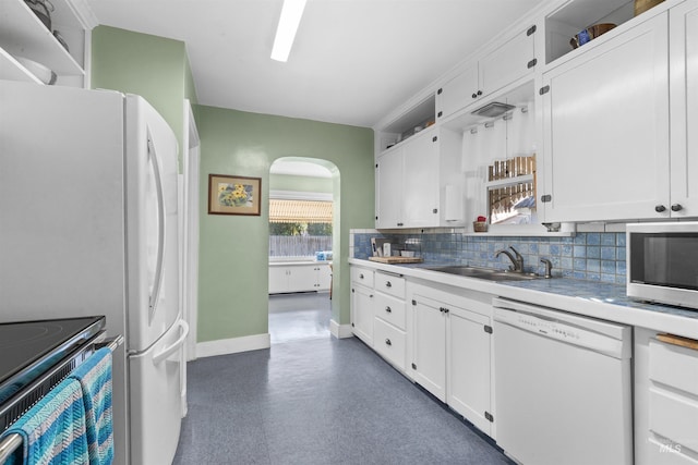 kitchen with arched walkways, dark floors, a sink, white cabinets, and dishwasher