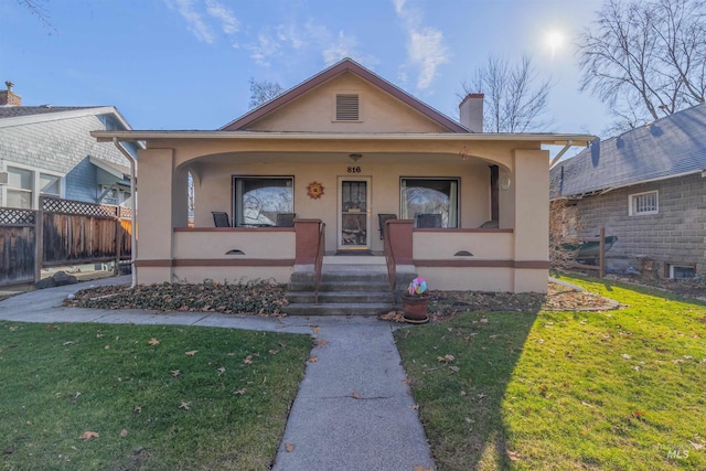 bungalow with covered porch, a chimney, a front lawn, and stucco siding