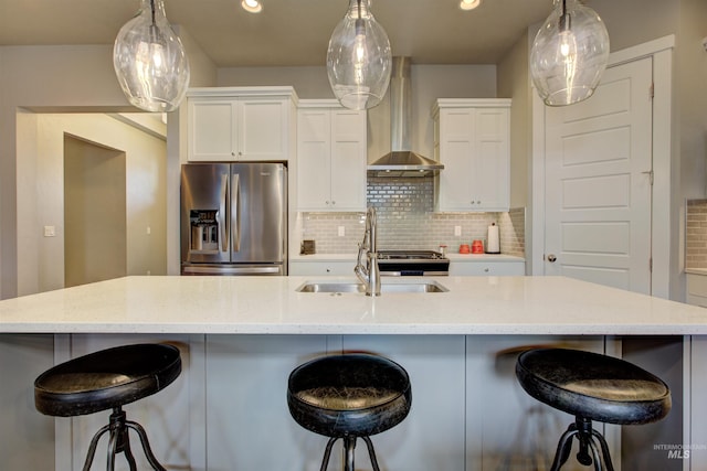 kitchen featuring white cabinetry, wall chimney range hood, stainless steel fridge with ice dispenser, a large island with sink, and a breakfast bar area