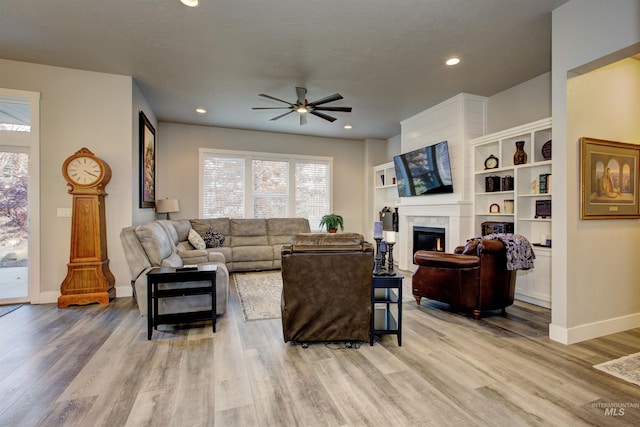 living room with a large fireplace, ceiling fan, and light hardwood / wood-style flooring