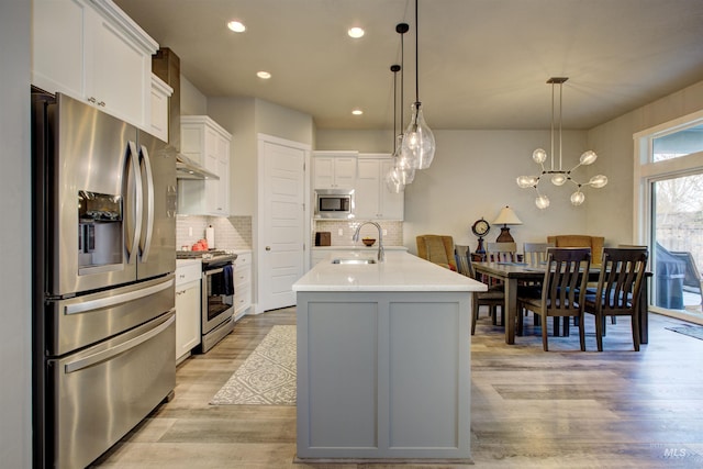 kitchen with stainless steel appliances, sink, white cabinetry, hanging light fixtures, and an island with sink