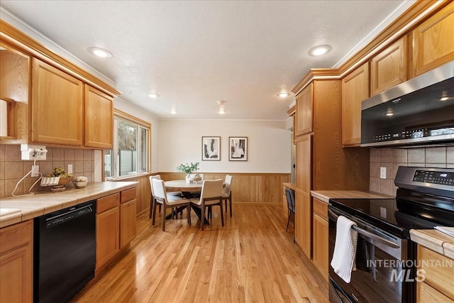 kitchen featuring tasteful backsplash, tile counters, wainscoting, stainless steel appliances, and light wood-type flooring