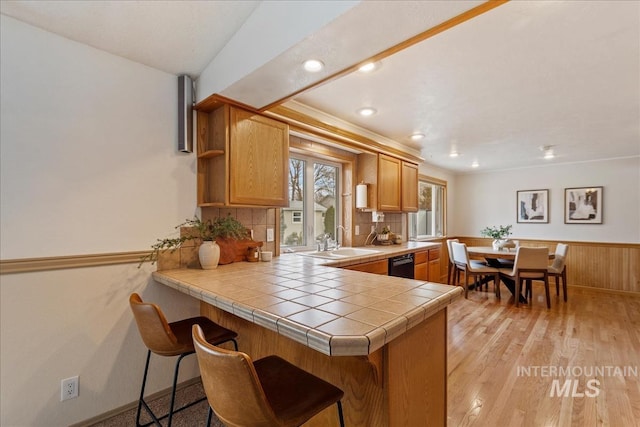 kitchen featuring a breakfast bar, light wood finished floors, a sink, dishwasher, and a peninsula