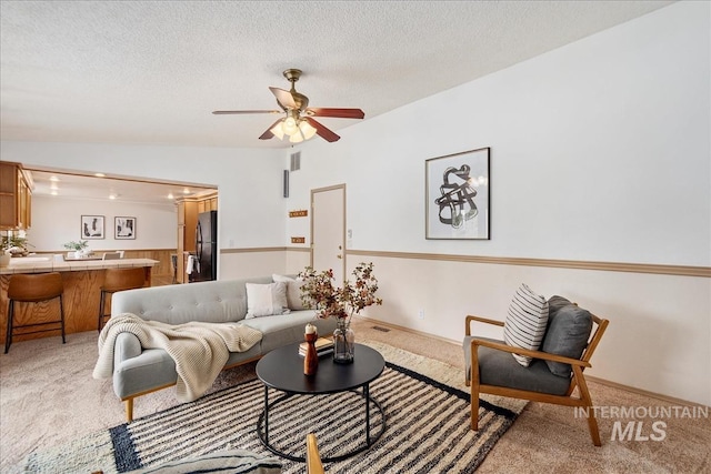 living room featuring a ceiling fan, lofted ceiling, light carpet, and a textured ceiling