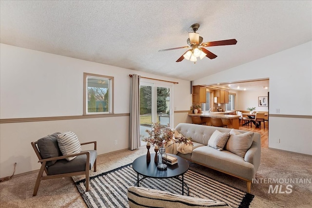 living area with vaulted ceiling, a textured ceiling, a ceiling fan, and light colored carpet