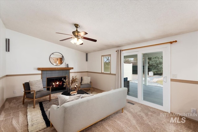 living area featuring a textured ceiling, ceiling fan, a fireplace, visible vents, and carpet