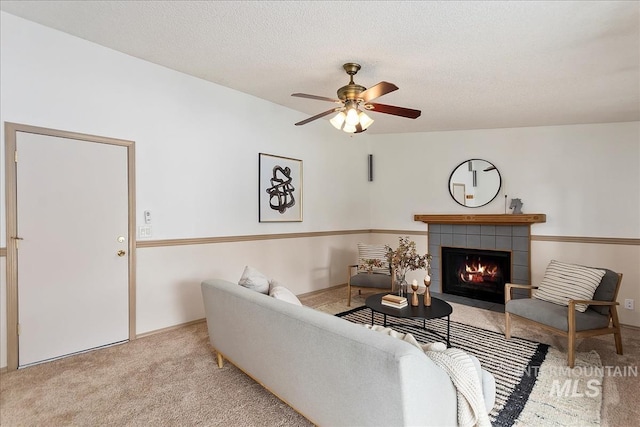 living area featuring carpet floors, ceiling fan, a textured ceiling, and a tile fireplace