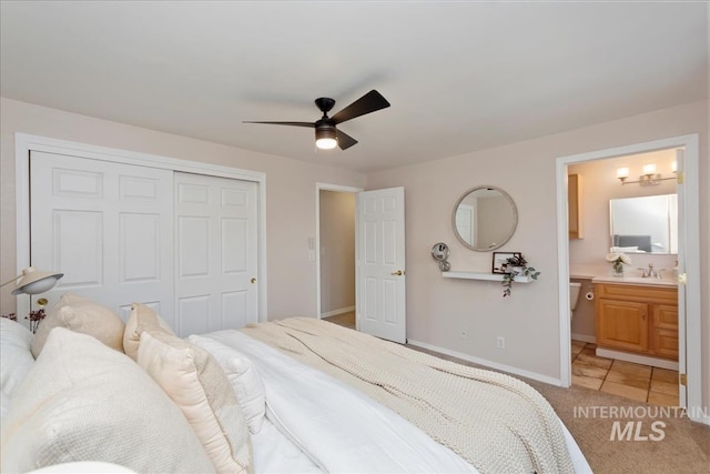 bedroom featuring light carpet, a closet, baseboards, ensuite bath, and a sink