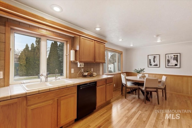 kitchen featuring dishwasher, tile countertops, a wainscoted wall, light wood-style floors, and a sink