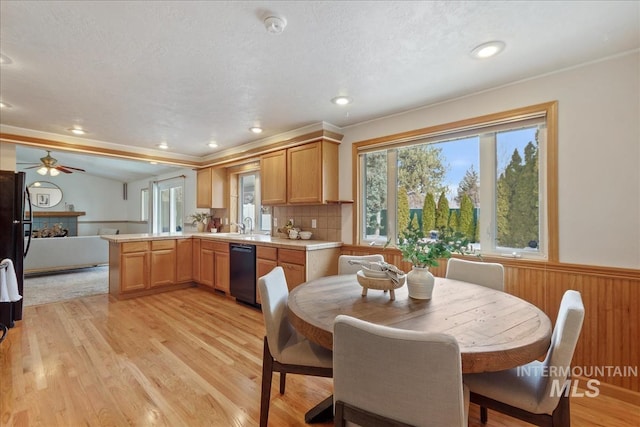 kitchen with black dishwasher, a wainscoted wall, a peninsula, light countertops, and light wood-style floors